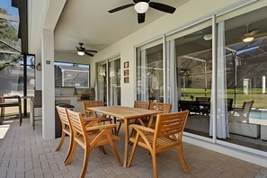 An outdoor patio with a wooden table and chairs, a ceiling fan, and a view of a backyard with a pool. - Windsor Hills 4BR Villa Private Pool + Game Room (Kissimmee)