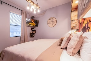 A bedroom with a bed, a TV mounted on the wall, a window with blinds, and a decorative wall piece. - Luxury 6BR Villa Prime Location, Pool & Cinema (Orlando)
