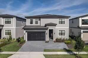 A modern two-story residential building with a central garage, surrounded by well-maintained landscaping and a clear sky. - Luxury 6BR Villa Prime Location, Pool & Cinema (Orlando)