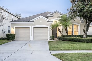 A modern two-story house with a garage, a well-maintained lawn, and a palm tree. - Windsor Hills 4BR Pool Home + Mario Game Room (Kissimmee)