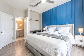 Ein modernes Schlafzimmer mit einem großen Bett, einem Nachttisch, einem Deckenventilator und einem durch eine offene Tür einsehbaren Badezimmer.