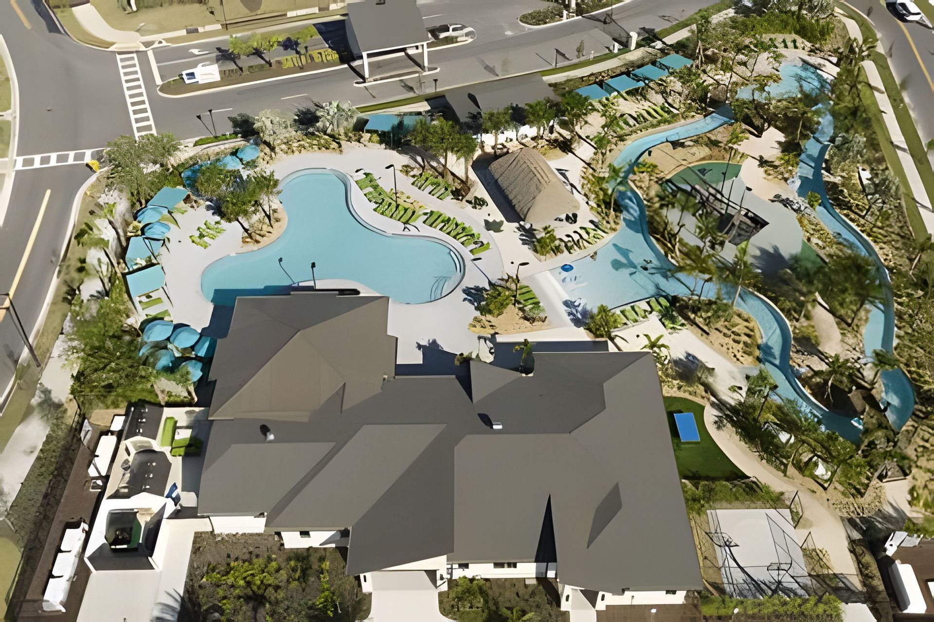 Luchtbeeld van een resort met een groot zwembad, aangelegde tuinen en een parkeerplaats.