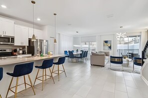 Een moderne keuken met witte kastjes, een centraal kookeiland met barkrukken, en een eethoek met blauwe stoelen.