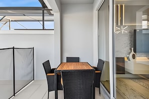 Een moderne eethoek buiten, met een houten tafel en zwarte stoelen, een glazen scheiding en uitzicht op de lucht.