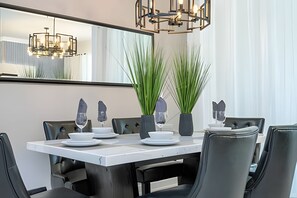 A modern dining area with a rectangular table, black chairs, and two tall green plants in vases. - Villa Smile - 4bd/3ba Storey Lake Luxury Themed (Kissimmee)