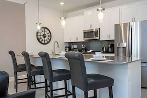 A modern kitchen with white cabinets, stainless steel appliances, and a central island with bar stools. - Villa Smile - 4bd/3ba Storey Lake Luxury Themed (Kissimmee)