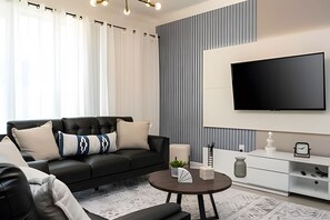A modern living room with a black leather sofa, a round coffee table, and a flat-screen TV mounted on the wall. - Villa Smile - 4bd/3ba Storey Lake Luxury Themed (Kissimmee)