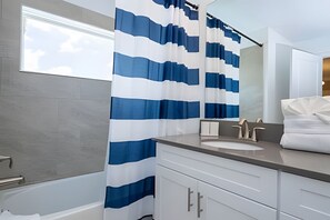 Un bagno con lavandino bianco, uno specchio e una tenda della doccia a righe blu e bianche.