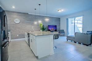 A modern kitchen with a central island, a dining area with a sofa, and a TV on the wall. - 4BR Storey Lake Townhome, Heated Pool (Kissimmee)