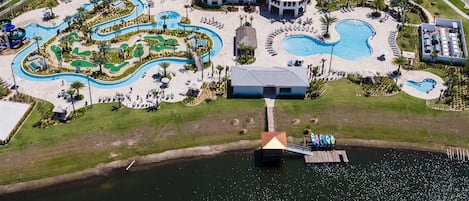 Vista aérea de un complejo turístico con múltiples piscinas, un parque acuático y un muelle que se adentra en un lago.