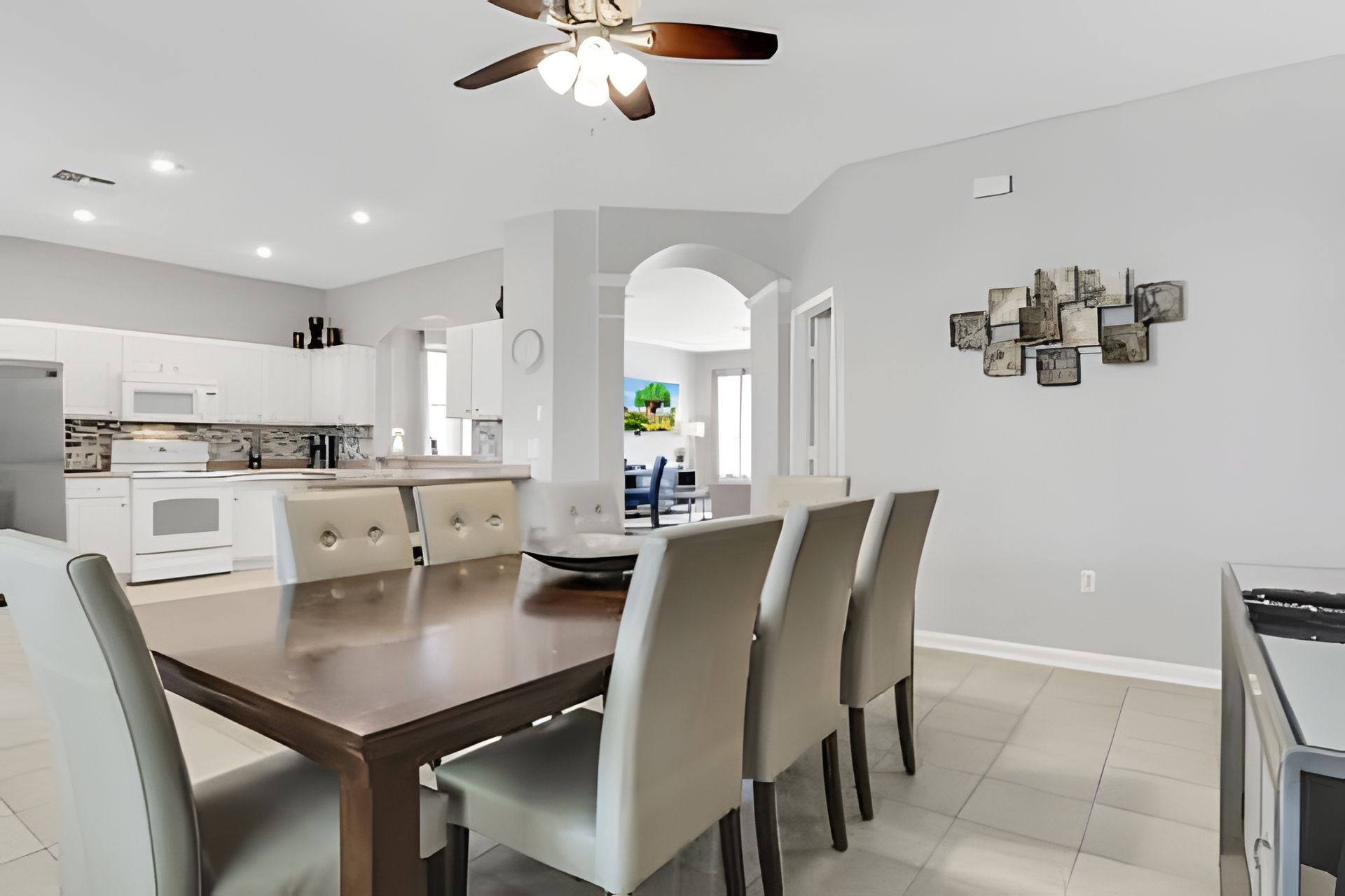 A modern kitchen with white cabinets, a built-in oven, and a dining area with a wooden table and chairs.