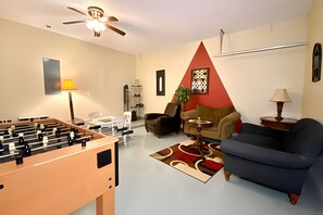 A living room with a foosball table, a sofa, a coffee table, and a TV. - 6bd/5.5ba Lux Pool Near Disney (Kissimmee)