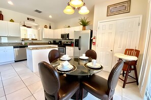 A modern kitchen with white cabinets, a central island, and a dining area with a glass table and leather chairs. - 6bd/5.5ba Lux Pool Near Disney (Kissimmee)