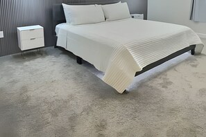 A neatly made bed with a white bedspread and pillows, a small bedside table, and a grey wall with vertical lines. - 5BR Storey Lake Home, Heated Pool (Kissimmee)