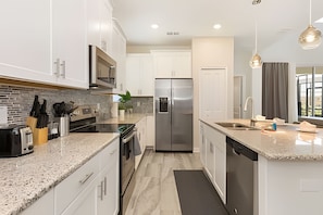 A modern kitchen with granite countertops, stainless steel appliances, and white cabinetry. - Resort Villa With Heated Pool and Ping Pong Table (Kissimmee)
