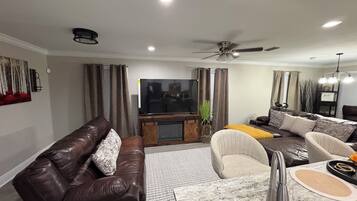 En moderne stue med en lædersofa, et spisebord med stole, et fladskærms-tv og en loftsvifte.