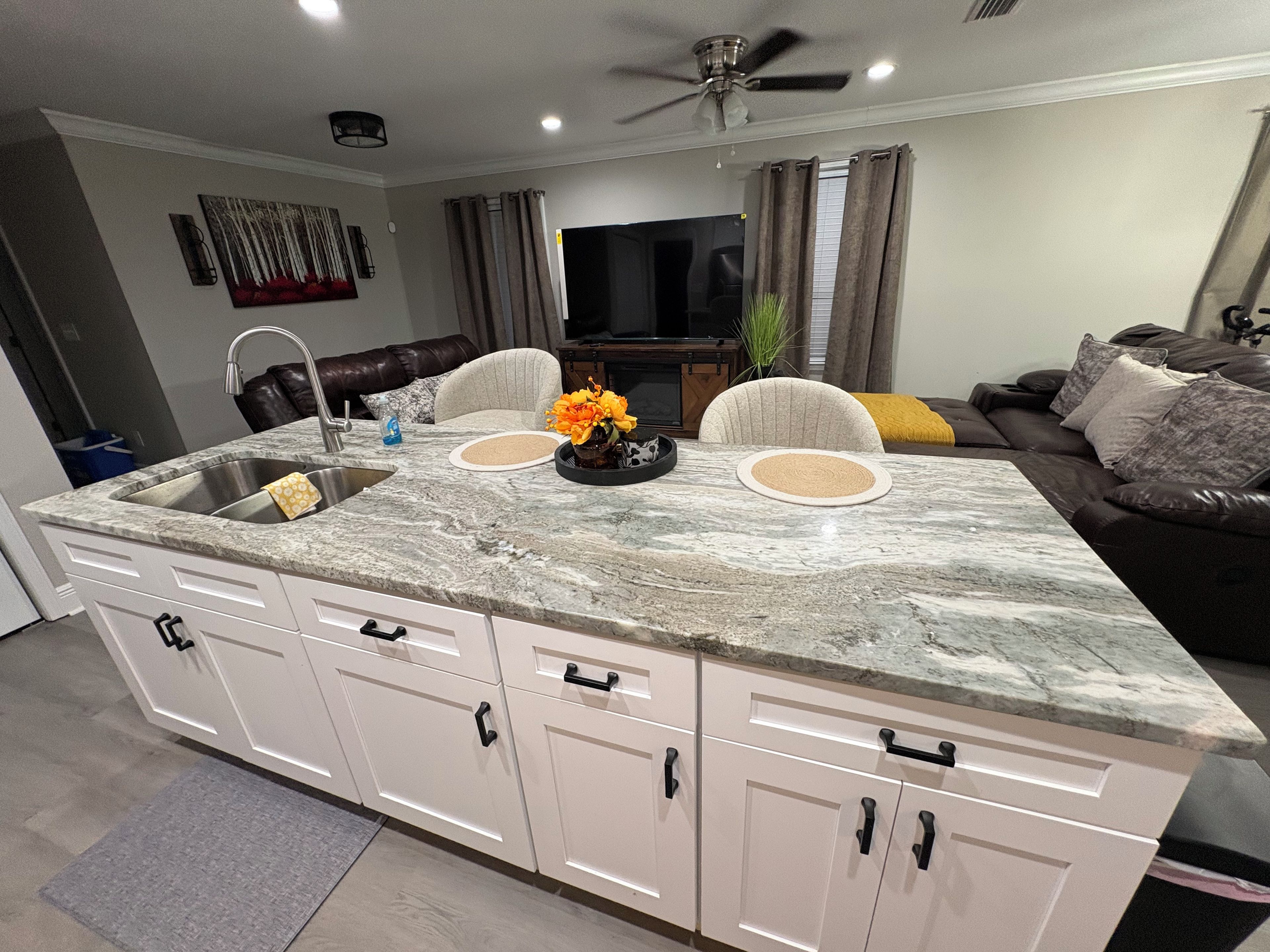 A kitchen with a marble countertop, white cabinets, a built-in sink, and a ceiling fan.