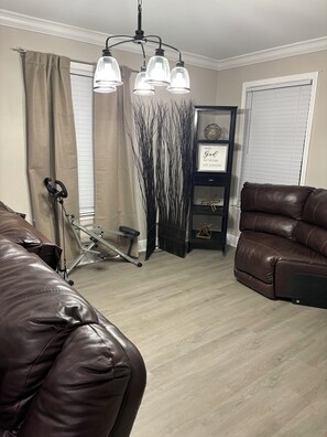 A living room with a brown leather sofa, a black leather chair, a standing exercise bike, and a chandelier with three lights. - 3-bedroom house in adorable Wilmer with cool AC breeze (Wilmer)