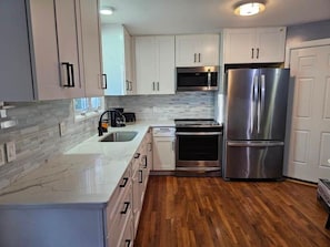 Cocina moderna con armarios blancos, electrodomésticos de acero inoxidable y piso de madera.