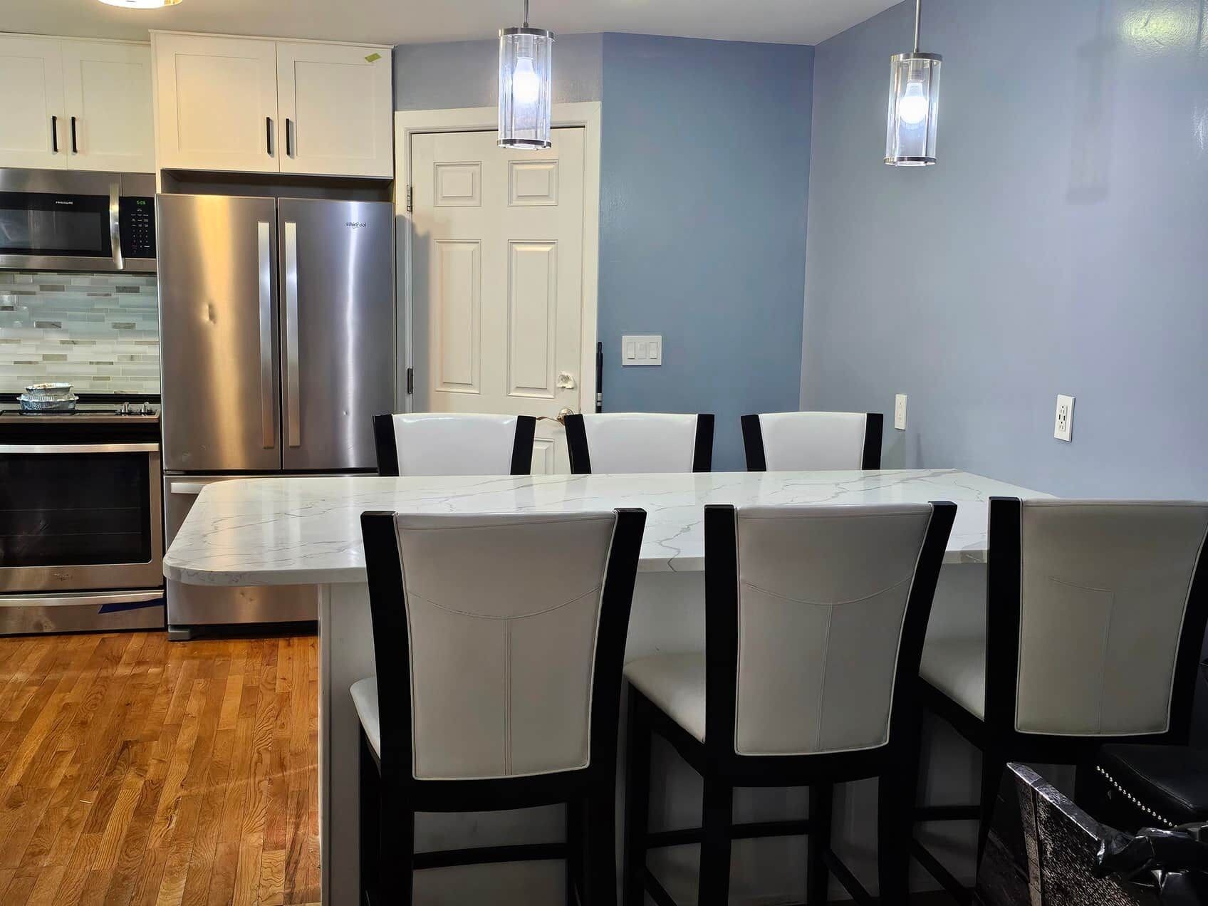 A modern kitchen with stainless steel appliances, a marble countertop, and a dining area with white chairs.