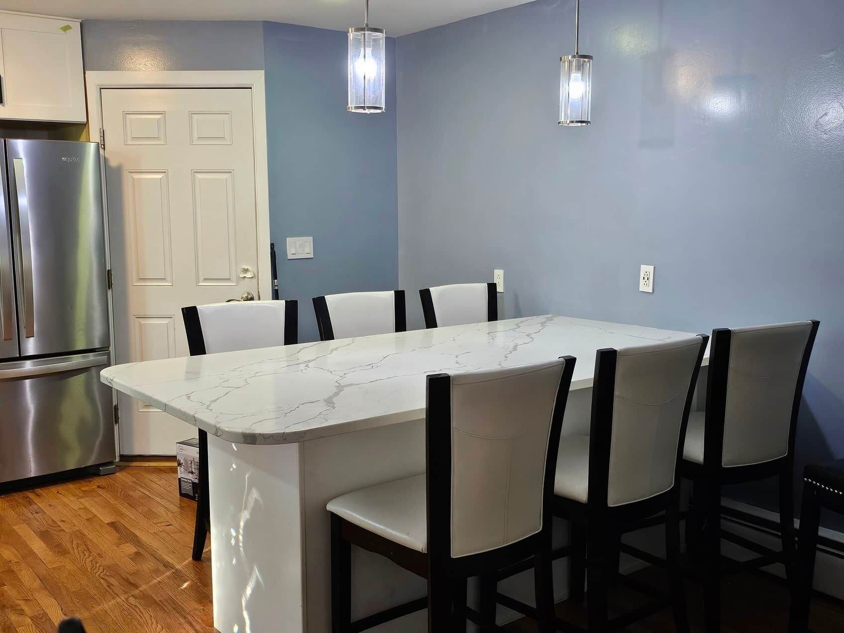 Une cuisine dotée d’un îlot en marbre, de chaises blanches et de luminaires suspendus.
