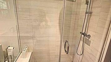 Un box de ducha con paredes de vidrio, un piso con estampado de espiga y un cabezal de ducha de mano, junto con un panel de control en la pared.