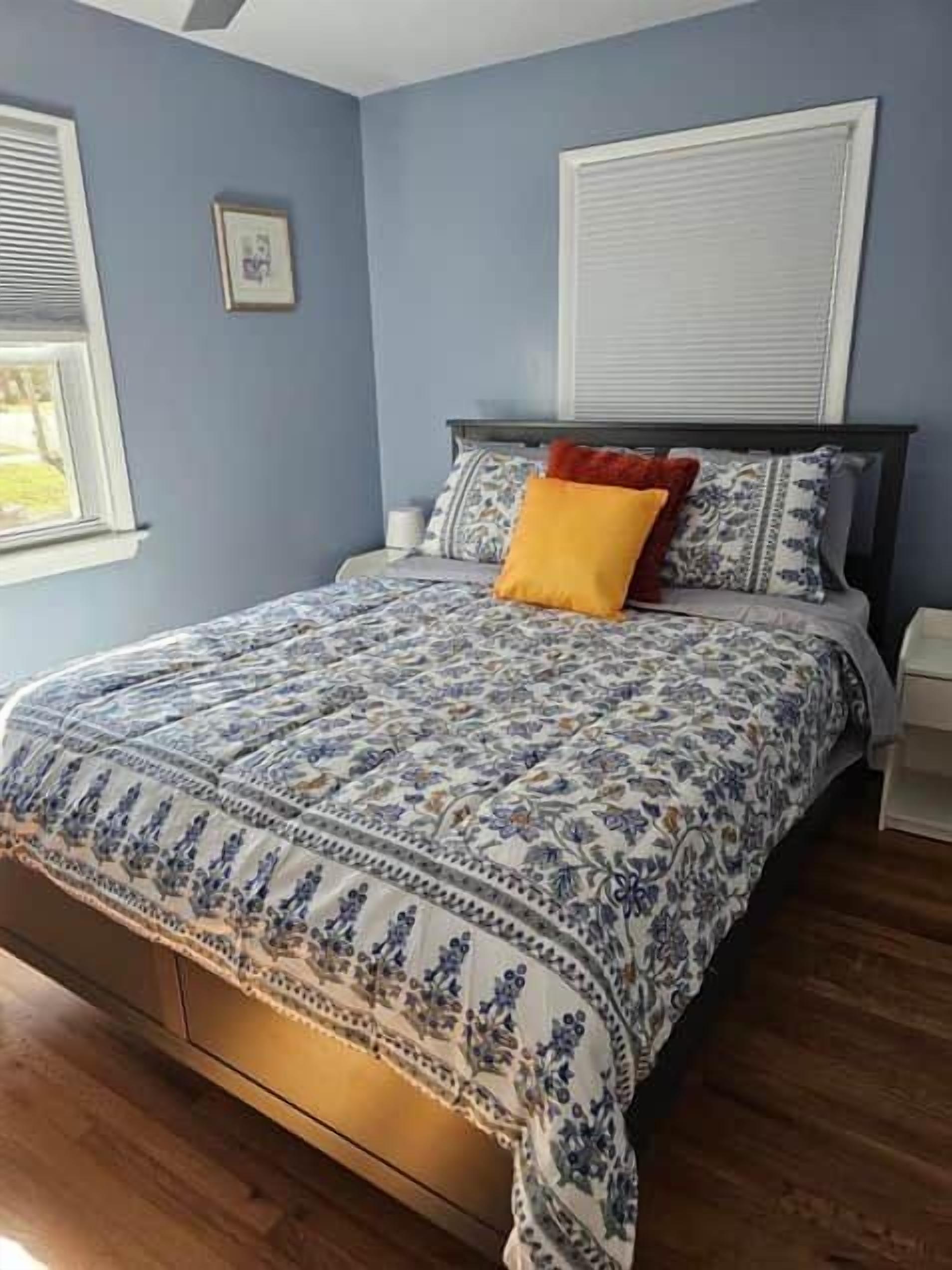 Une chambre à coucher avec un lit, une table de chevet, une fenêtre et un tableau accroché au mur.