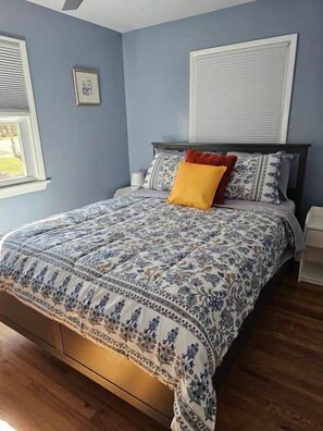 Een slaapkamer met een bed, een nachtkastje, een raam en een aan de muur hangend schilderij.