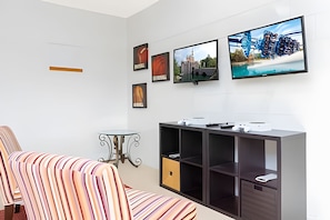 A modern living room with a striped sofa, a small round table, and a cabinet with shelves. There are three framed pictures on the wall. - Disney 4BR Home + Pool & Themed Bedrooms (Kissimmee)