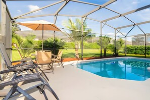 A covered outdoor pool area with a clear view of the surrounding greenery and a poolside seating area. - Disney 4BR Home + Pool & Themed Bedrooms (Kissimmee)