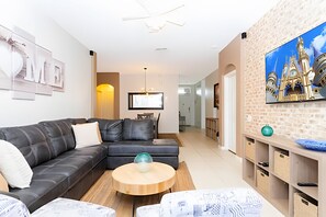 Ein modernes Wohnzimmer mit einer Eckcouch, einem runden Couchtisch aus Holz und einem an der Wand montierten Fernseher.