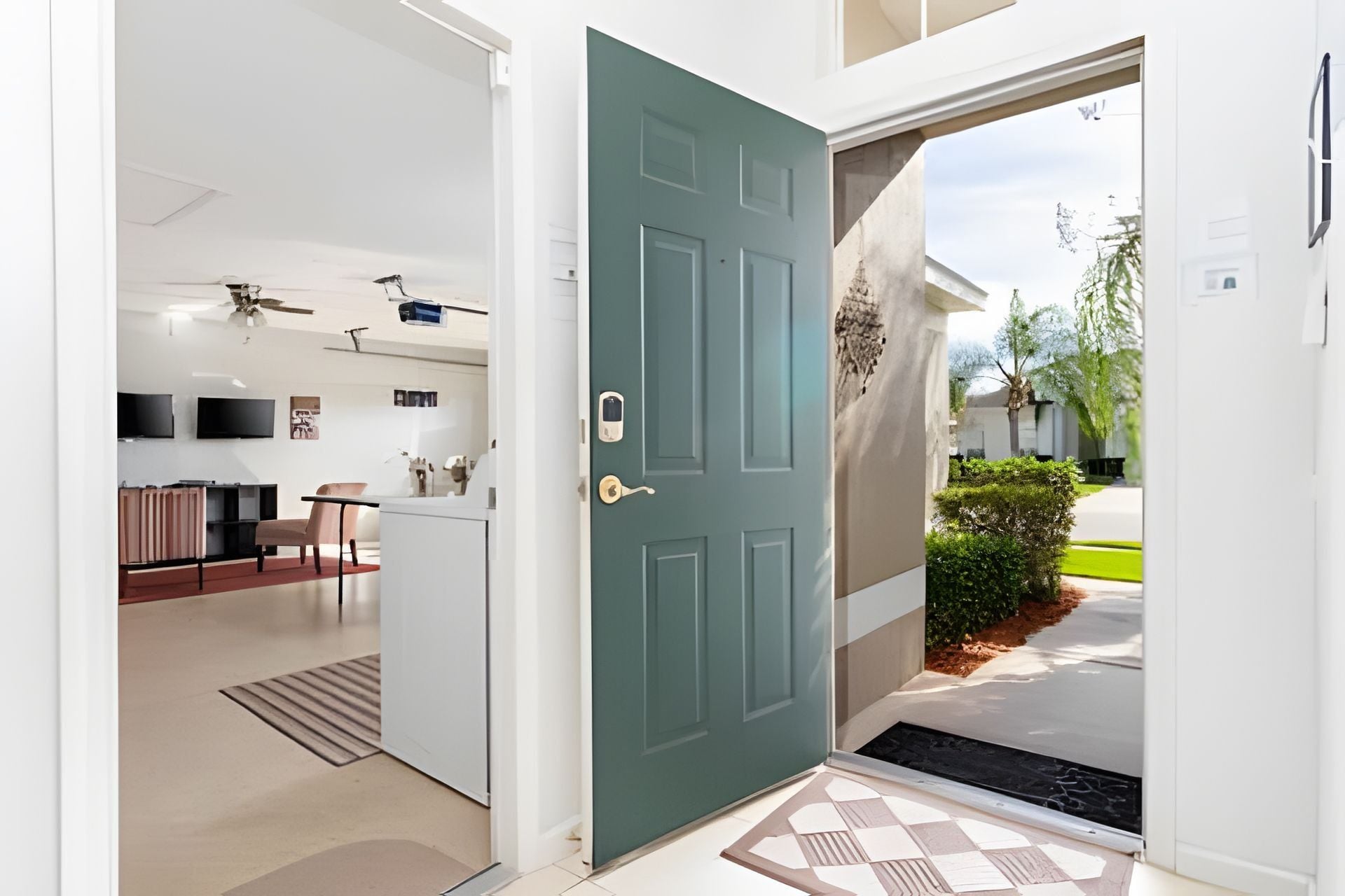 Un interior moderno con una puerta verde azulado, una zona de cocina con comedor y vista a una calle residencial.