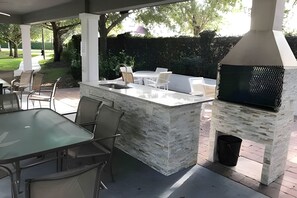 Eine Außenpatio mit Stein-Barbecue, Sitzbereich und einem Glastisch.