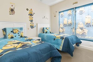 Ein Schlafzimmer mit zwei Betten, beide mit einer blauen Decke mit Minion-Motiven. Die Wände sind mit Minion-Aufklebern dekoriert und ein großes Fenster bietet Blick auf die Stadt.