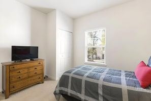 Ein Schlafzimmer mit einem Bett, einer Kommode, einem Fernseher auf der Kommode und einem Fenster mit Jalousien.