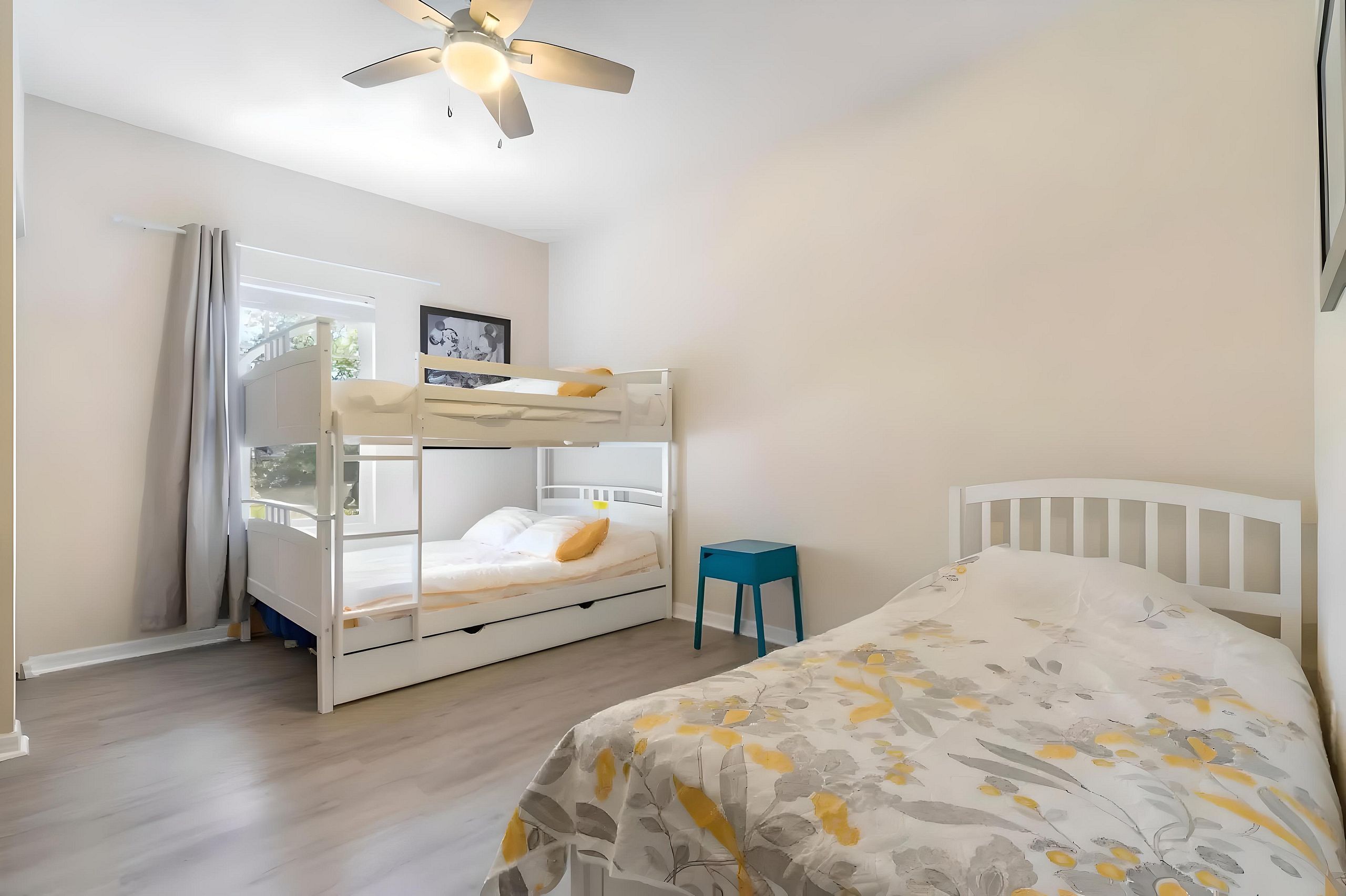 A room with bunk beds, a single bed, a ceiling fan, and a small stool.