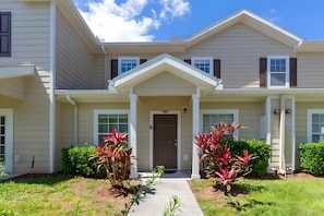 A two-story building with a central entrance, a covered porch, and a small garden with plants. - 3BR Home With Resort Pool & Game Room (Kissimmee)