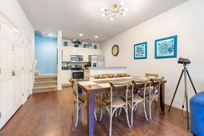 A modern kitchen with white cabinets, a dining area with a wooden table and chairs, a clock on the wall, and a camera on a tripod. - 3BR Home With Resort Pool & Game Room (Kissimmee)