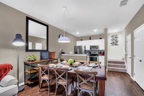 A modern kitchen with white cabinets, a dining area with wooden chairs, and a staircase leading to another level. - 3BR West Lucaya Home Near Disney (Kissimmee)