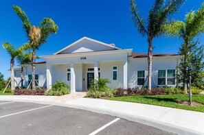 A modern building with a white facade, numbered 3241, featuring a symmetrical entrance with columns, surrounded by landscaped greenery and palm trees. - 3BR West Lucaya Home Near Disney (Kissimmee)