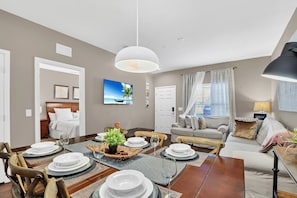 A dining area with a wooden table set for four, a sofa, and a bed in the background. - 3BR West Lucaya Home Near Disney (Kissimmee)