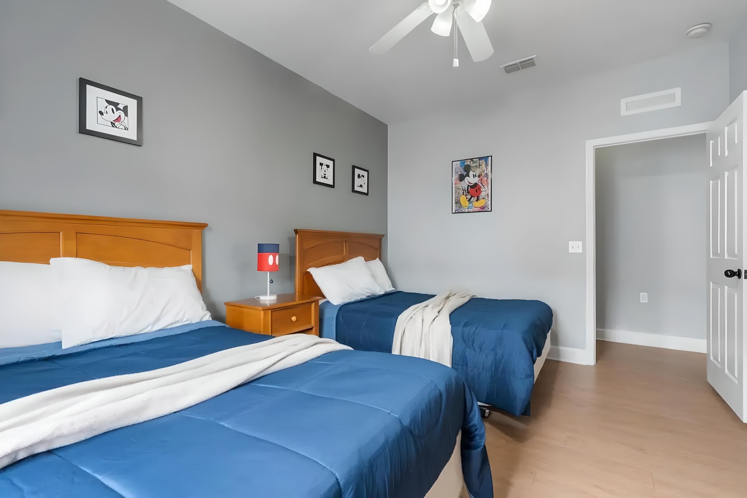 A hotel room with two beds, a ceiling fan, and framed artwork on the walls.