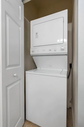 A compact laundry room with a stacked washer and dryer. - 3BR Home With Private Pool Near Disney (Kissimmee)