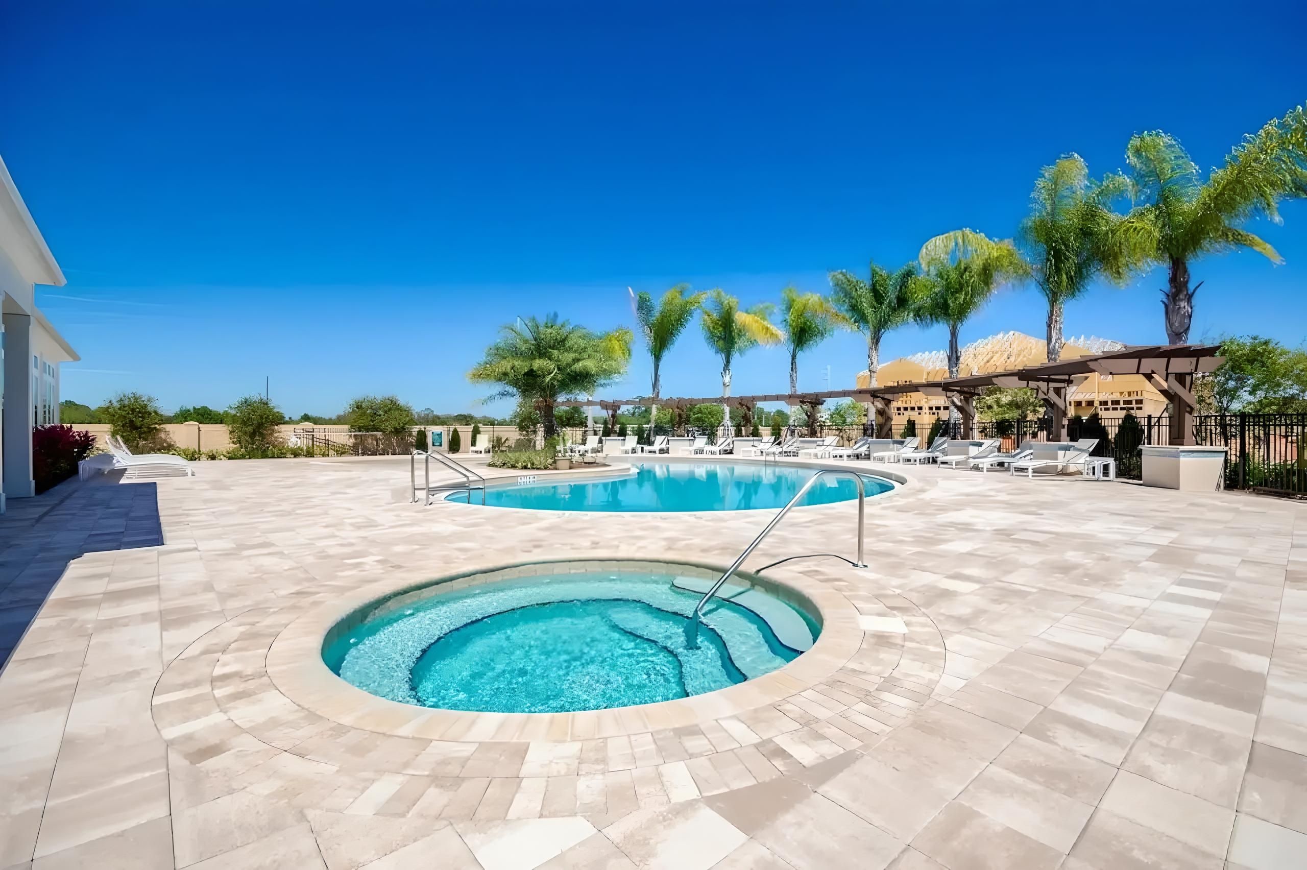 Un espace piscine comprenant un jacuzzi, des chaises longues et des palmiers.