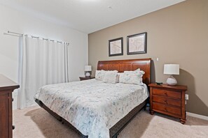 A bedroom with a large bed, two nightstands, a wooden dresser, and a white curtain. - Amazing 4bdr House Near Disney (Kissimmee)