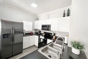 A modern kitchen with white cabinets, stainless steel appliances, and a black countertop. - 4BR Themed Townhome in Lucaya Resort (Kissimmee)