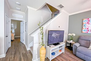 Una sala de estar moderna con una escalera, un televisor de pantalla plana, un sofá gris y una pequeña mesita de noche con un florero.