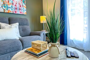 A living room with a grey sofa, a coffee table, a potted plant, a decorative pitcher, and a stack of books. - 4BR Themed Townhome in Lucaya Resort (Kissimmee)