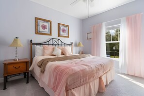 Ein Schlafzimmer mit einem Bett, zwei Nachttischen, einem Fenster mit Vorhängen und zwei gerahmten Bildern an der Wand.