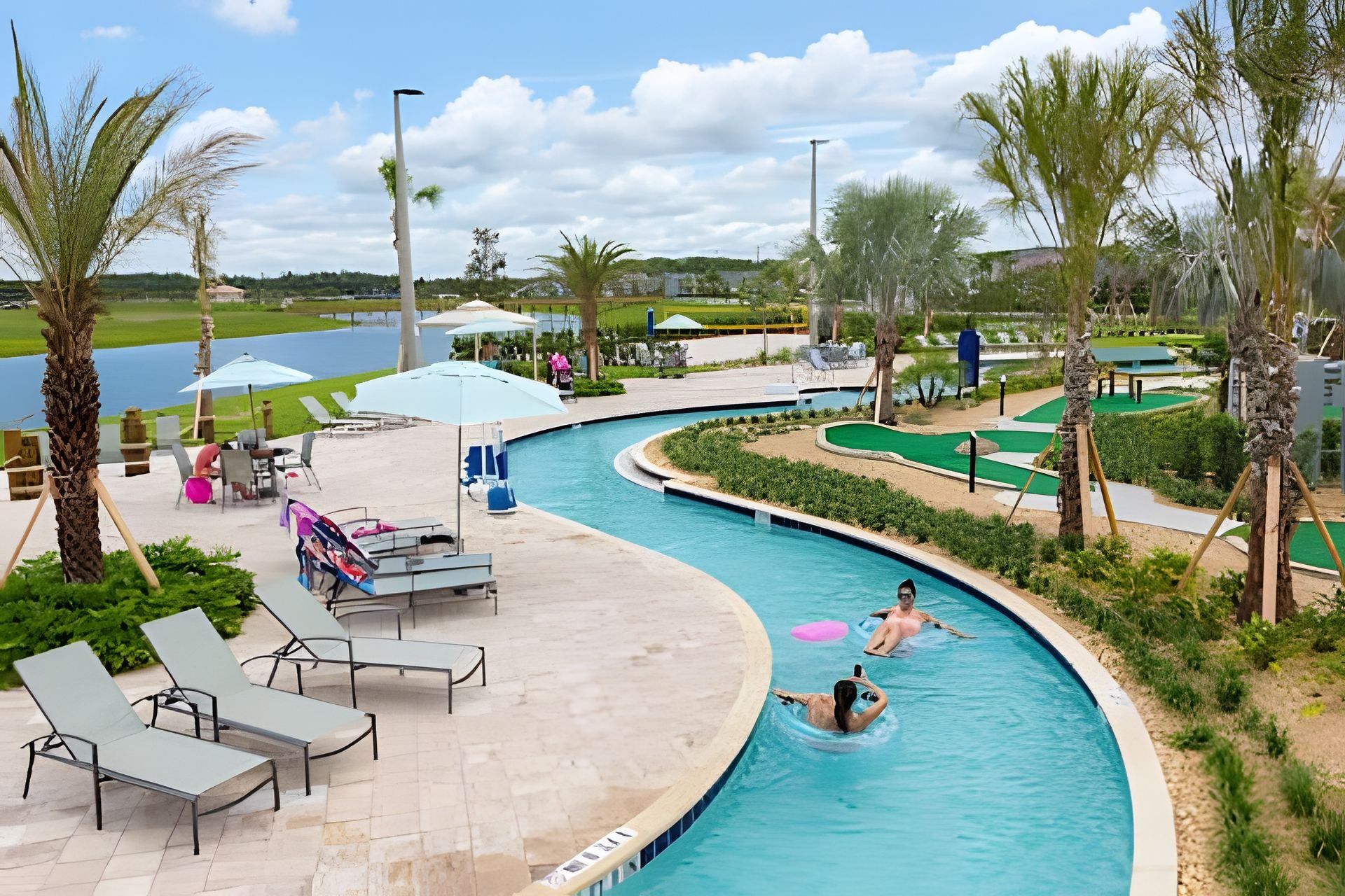 A swimming pool with lounge chairs and umbrellas, surrounded by palm trees and a golf course in the background.
